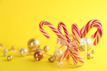Candy canes and Christmas balls on yellow background, space for text
