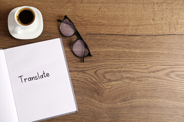 Notebook with written word Translate, cup of coffee and eyeglasses on wooden table, flat lay. Space...