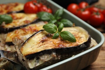 Spatula with piece of delicious eggplant lasagna over baking dish at table, closeup