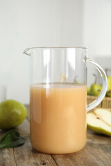Fresh pear juice in glass jug on wooden table, closeup