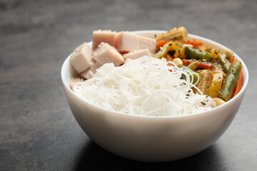 Tasty cooked rice noodles with chicken and vegetables on grey table