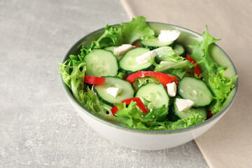 Delicious salad with cucumbers, red bell pepper and feta cheese in bowl on light grey table, closeup
