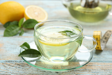 Glass cup of diet herbal tea with green leaves and lemon on wooden table