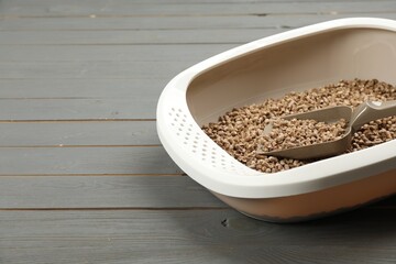 Cat litter tray with filler and scoop on grey wooden floor, closeup. Space for text
