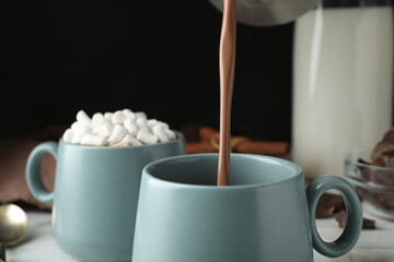 Pouring hot cocoa drink into cup on black background, closeup