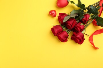 Beautiful red roses and decorative hearts on yellow background, flat lay with space for text....