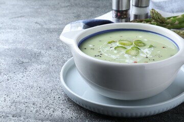 Bowl of delicious asparagus soup on grey table, space for text