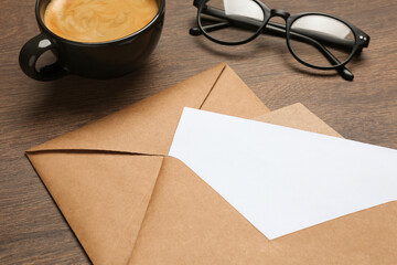Envelopes with blank paper card, cup of coffee and glasses on wooden table, closeup