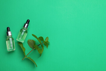 Bottles of essential oil and mint on green background, flat lay. Space for text
