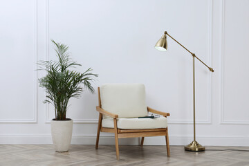 Stylish room interior with lamp, armchair and houseplant near white wall