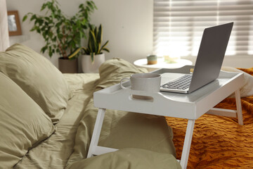 White tray with modern laptop and cup of aromatic drink on bed indoors, space for text