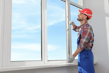 Worker in uniform installing plastic window indoors