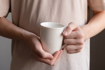 Mug in hands close-up. A young guy without a face in a light T-shirt holds a white mug.