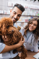 Blurred muslim man holding poodle near veterinarian in pet shop