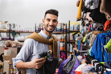 Smiling muslim man holding animal jackets and looking at camera in pet shop
