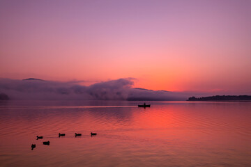 Zjawiskowy wschód słońca nad jeziorem i rybak w łodzi