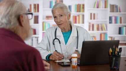 Mature senior female doctor talking to male patient in modern clinic with library background.