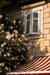 Fototapeta na wymiar Beautiful mediterranean house with white window shutters and red and white shade and wonderful oleander tree on the side