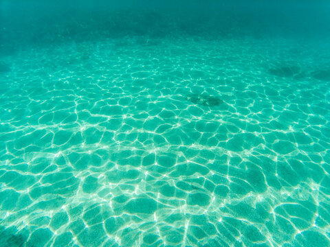 Underwater picture of sand sea bottom with waves refraction visible on the sea floor