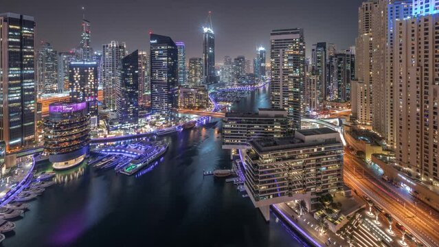 Aerial view to Dubai marina skyscrapers and jbr towers around canal with floating boats day to night transition timelapse. White boats are parked in yacht club after sunset