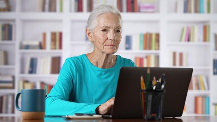 Smiling mature business woman using laptop computer sits at home office. Happy senior older employee 60s 70s businesswoman executive working typing on pc.