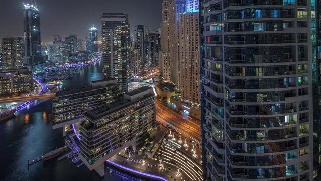 Panorama showing aerial view to Dubai marina illuminated skyscrapers around canal with floating yachts night timelapse. Towers in jlt and jbr districts. White boats are parked in yacht club