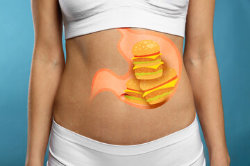 Woman with image of stomach full of junk food drawn on her belly against light blue background,...