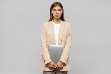Portrait of shy student girl feeling nervous standing isolated on gray background with laptop