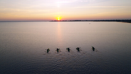 Five kayaks with people are sailing towards the sunrise. A large expanse of lake water. Summer...