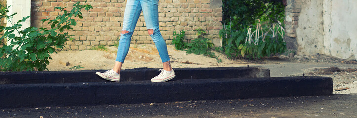 Long legs in sneakers and jeans of the young woman walking in an abandoned building.