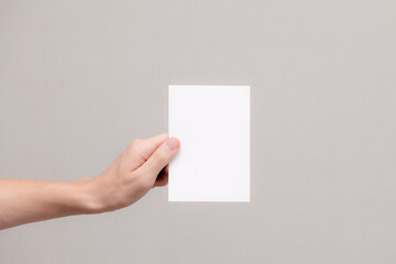 White business card in hand on a gray background. Close-up. Place for writing text. Layout.