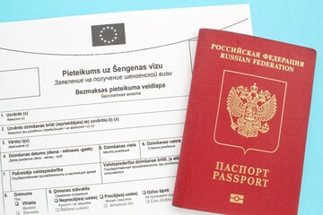Schengen visa application form in Russian and Latvian language and passport on blue background. Prohibition and suspension of visas for tourists to travel to European Union and Baltic States concept