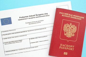 Schengen visa application form in Russian and Lithuanian language and passport on blue background. Prohibition and suspension of visas for tourists travel to European Union and Baltic States concept