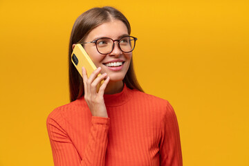 Portrait of woman in glasses talking on phone isolated on yellow background