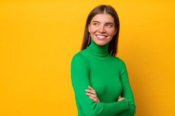 Obraz premium Studio portrait of smiling dreamy pensive woman with crossed arms standing on yellow background