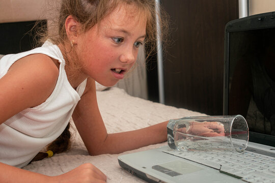 The Girl Accidentally Knocked Over A Glass Of Water On The Laptop. The Child Poured Water On The Computer Keyboard.