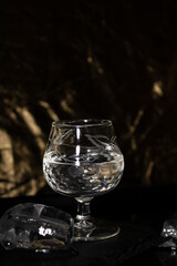 glass filled with clear liquor anis, tequila, rum, etc. on a slate stone and a water base with golden reflections with two ice cubes, one in the water and the other in the stone. with space for text, 