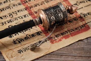 Tibetan hand prayer wheel with an old tibetan manuscript on wooden surface