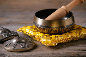 Tibetan singing bowl with engraved sanskrit mantra „Om Mani Padme Hum“ and cymbals on a wooden table. The text on the singing bowl is a famous sanskrit mantra which means „The jewel is in the lotus“