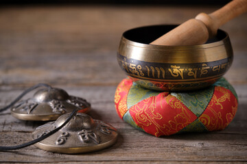 Tibetan singing bowl with engraved mantra „Om Mani Padme Hum“ and cymbals on a wooden table....