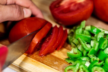 Slicing Tomatos and green sweet peppers on wooden board with a knife