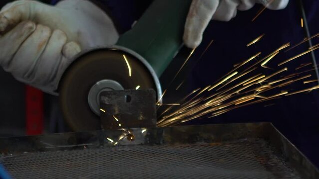 Slowmotion of worker in special clothes and gloves grinding metal with a circular saw in his workshop, bright sparks of metalworking fly in different directions.