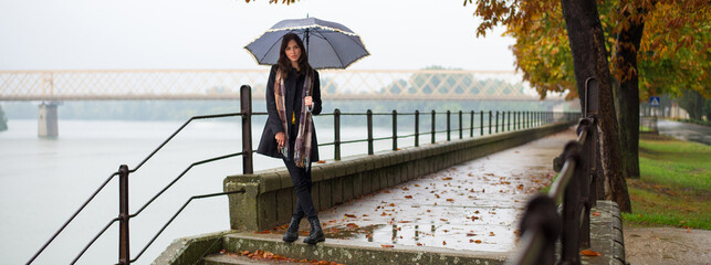 Young woman with umbrella walking in the autumn rain