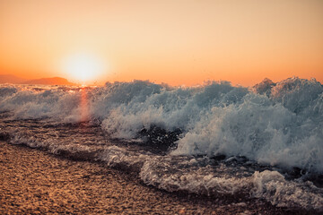 Beautiful abstract nature background with sea orange sunset on the coastline and splashing waves on the seashore