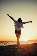 Cheerful young woman enjoying freedom on vacation on the seaside holding arms open on sunset