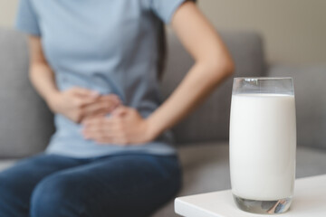 lactose intolerance concept. A glass of milk is on the table and have stomachache woman on sofa