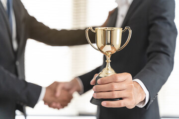 The hands of an employee receiving a golden cup reward from the company manager represent his...