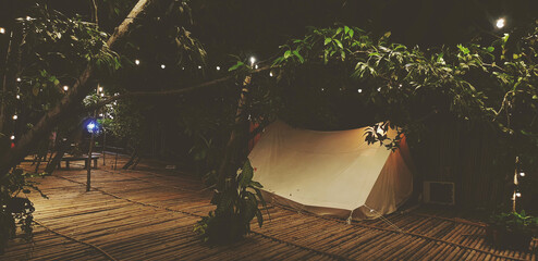 White tent on dry bamboo floor with tree and lighting decorated at night in vintage tone. Camping...