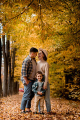 Portrait of happy young family on the background of autumn park. Mom, dad and son are smiling. Family autumn photo shoot