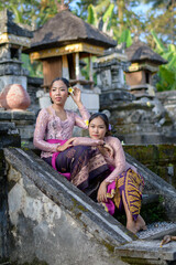 Portrait two Bali girls in colorful traditional clothes on the steps in old temple.